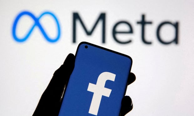 a smartphone displaying the facebook logo is held up against a display of the meta logo on a white background