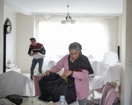 A man and woman look through their belongings in a living room. White blankets have been placed over furniture