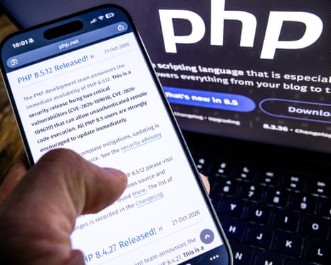 A close-up of a mobile phone showing PHP's patch release, and behind it the organisation's logo on a laptop screen