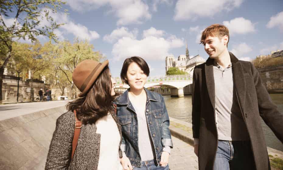 Three young friends taking a promenade in Paris, France along the River Seine, with Notre Dame cathedral in the background