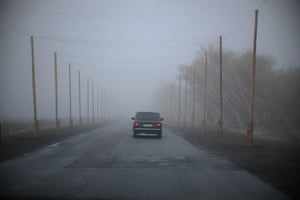 A car driving away along a road, in mist, with nets surrounding the road