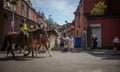 People stand at the end of a row of terraced houses as two police officers ride past on horses