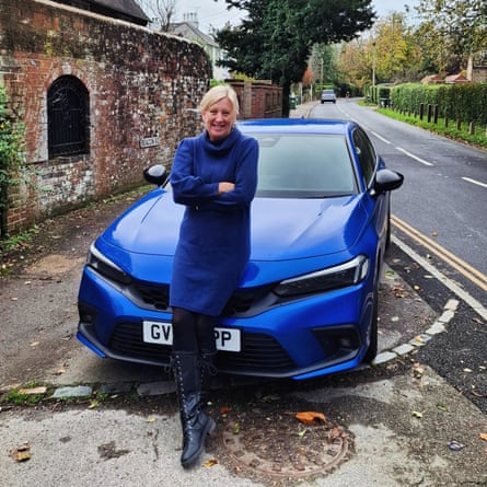 Blonde woman in blue coat sitting on the bonnet of a blue car