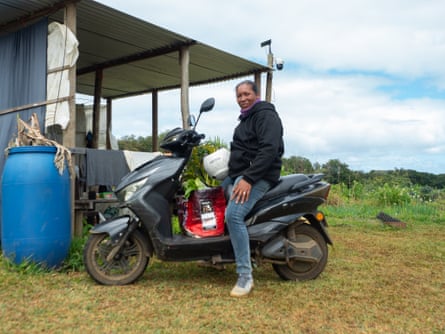A woman sits on a moped outside a farm outhouse