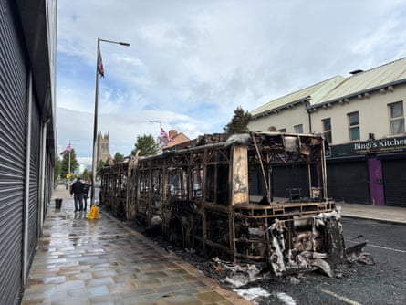 The skeleton of burned bus parked beside a row of shops