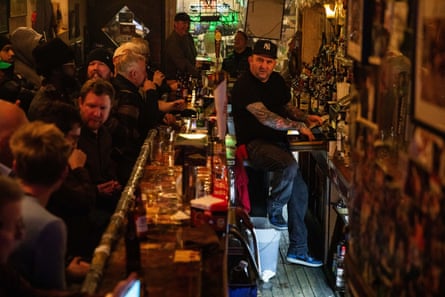 a bartender sits on the edge of a fridge as he holds money at a cash register