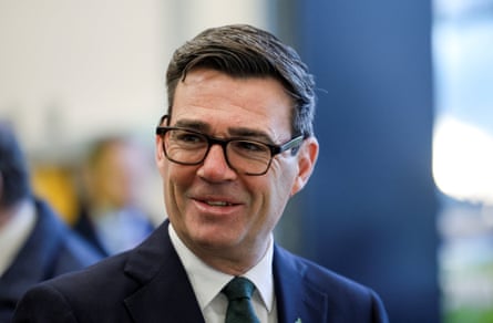 Andy Burnham smiles, wearing glasses and a dark suit with a green tie