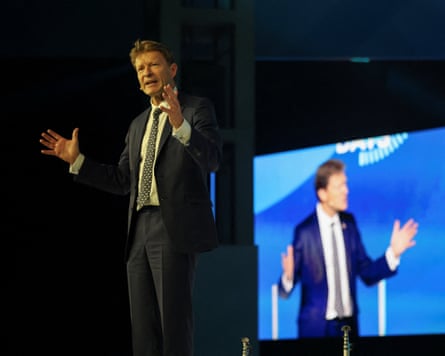 Richard Tice gesticulates on stage, with his speech projected on a large screen behind him