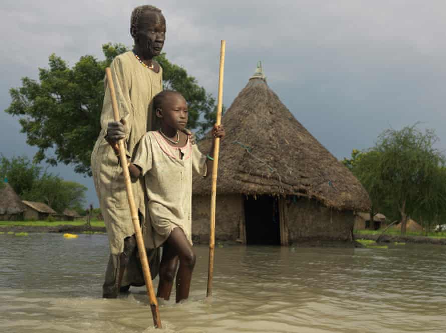David Deng, who is blind, navigates his way through the floods with the help of his nine-year-old granddaughter, Angelina Nyagok.