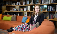 Debbie Weinstein sits on a long, curved orange couch in front of a wall of bookshelves.