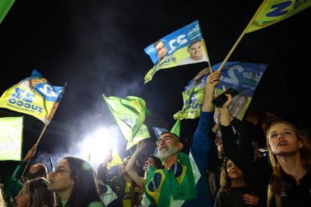 People stand in the dark waving flags with pictures of Bolsonaro and wearing green and yellow colours.
