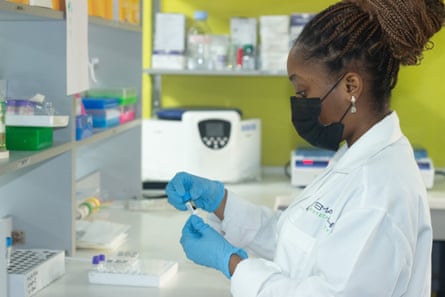 A young African woman in a white coat working with test tubes in a lab