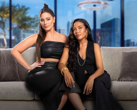 Ashley Graham and Emma Grede in black outfits on a sofa.