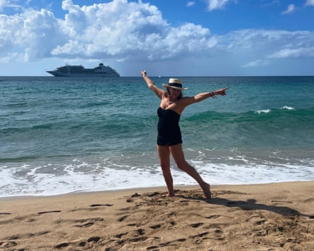 A woman poses happily on a beach in the Caribbean. In the background a cruise ship passes by.