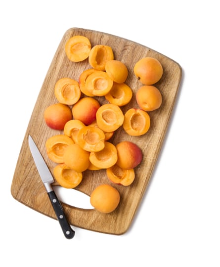 A chopping board with lots of sliced apricots and a knife.
