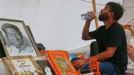 Abhijeet Dipke drinks from a bottle of water next to a portrait of hunger-striking activist Sonam Wangchuk