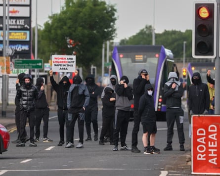 A group of men and boys wearing black and grey with their hoods up over their heads and their faces covered.