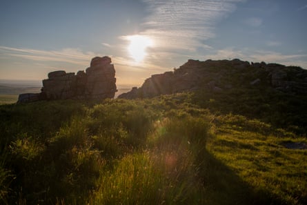 The sun is seen setting through a rock formation by close cropped tufts of grass.