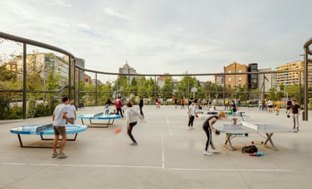 A group of people play table tennis on several tables outside.