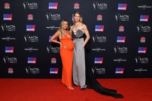 Channel V’s Renee Bargh in a bright orange gown posing with Christian Wilkins, who wears a crystal corset and dove grey palazzo pants