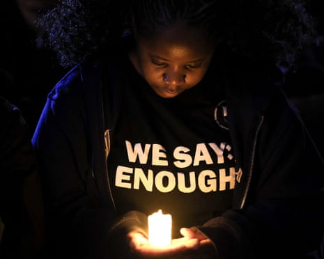 A student holds a glowing candle at a vigil, wearing a "We Say Enough" shirt