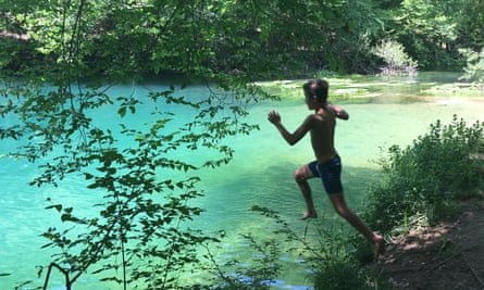 A little boy jumps off the bank into the clear water of the river.