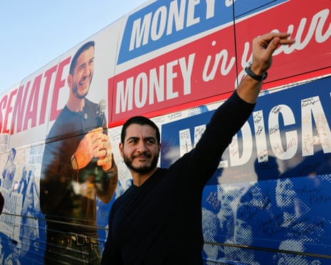 Abdul El-Sayed smiles and raises his hand beside his signed campaign bus