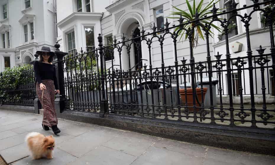 A woman walks her dog along a residential road in Kensington in London,