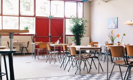 A dining area at De School club in Amsterdam. The daytime image shows desks and chairs used as places to dine in a large, communal room.