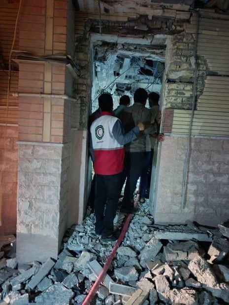 Half a dozen men stand at the doorway of a damaged building looking in.