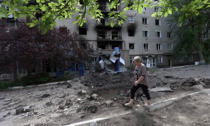 A woman walks past a shell crater in front of a damaged residential building in the town of Siversk, Donetsk region, on June 23, 2022, amid Russia’s military invasion launched on Ukraine.