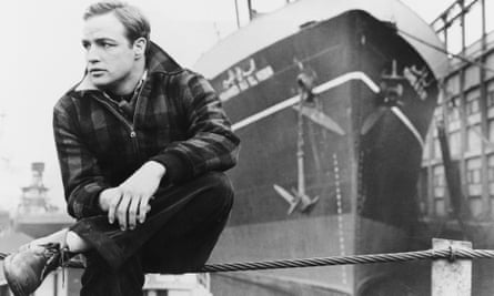 Marlon Brando photographié en noir et blanc, dans On the Waterfront, 1954, assis sur la rampe devant un grand navire.