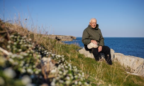 Author and naturalist Andrew Cleave sat on a group of rocks at Portland Bill, Dorset, UK on a blue-sky day.