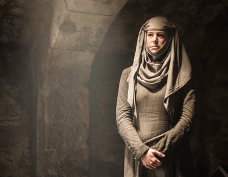 As Septa Unella in Game of Thrones. She is wearing a brown headscarf which is draped round her chin and over her shoulders and wearing a brown dress