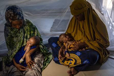 Displaced Somali women hold their severely malnourished babies in small huts