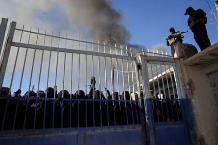 Women gather at the gates of the camp as guards stand watch above