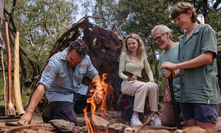 Image of man demonstrating how to start a campfire while three people watch him.
