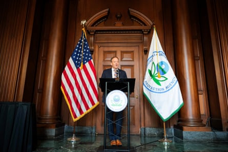 man in suit speaks into microphone at lectern with an american flag and flag for environmental protection agency behind him