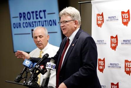 man talks in front of sign that says 'yes on 1 - protect our constitution'