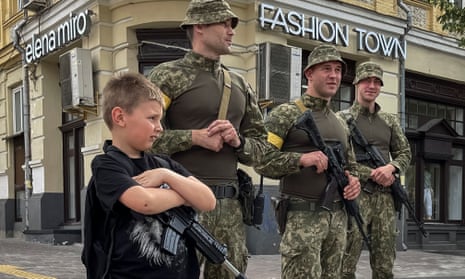 A boy with a toy machine gun stands near Ukrainian servicemen as they patrol central Kyiv.