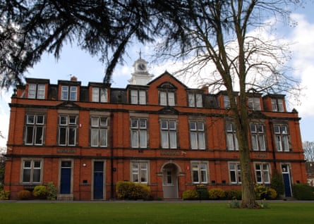 An imposing red-brick building set with a lawn and tall trees in the foreground