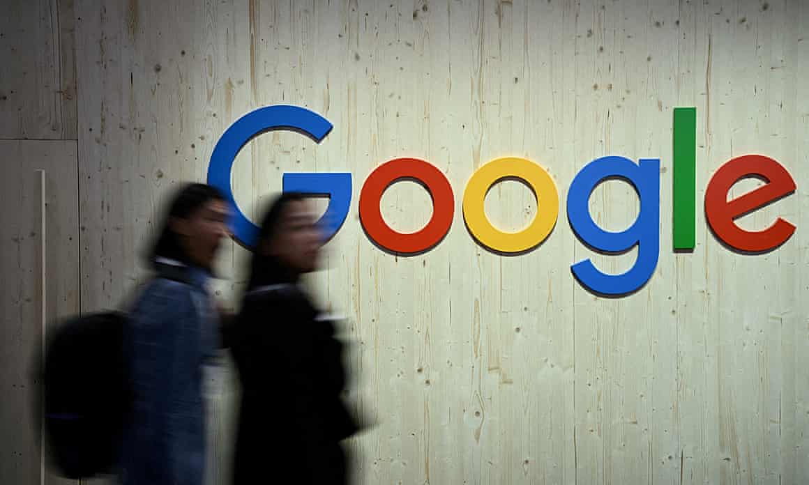 Two people walking past a Google sign in an office.
