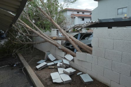 Toppled tree damages stone wall in parking lot outside apartment complex