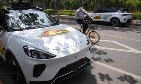 A man on a bicycle rides past self-driving taxis   in Beijing
