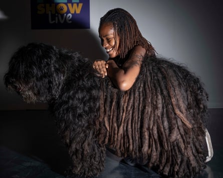 A smiling woman kneels beside a shaggy brown dog.