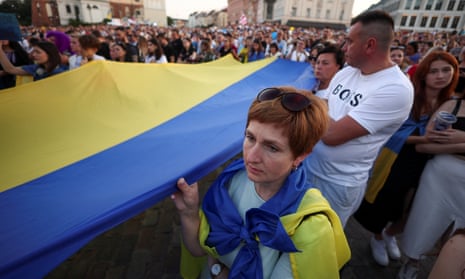 A crowd of people in square carry a large Ukrainian flag