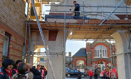 A man walks along scaffolding on the arch as young people in hi-vis tabards look on