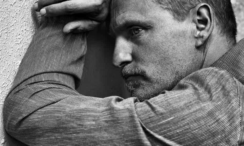 Woody Harrelson leaning against a tree