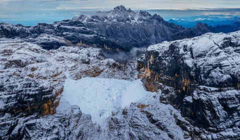 Snow-covered Puncak Jaya with exposed rock faces and glacial ice surrounding a deep valley