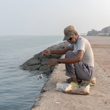 Man crouched down reeling in line at water’s edge